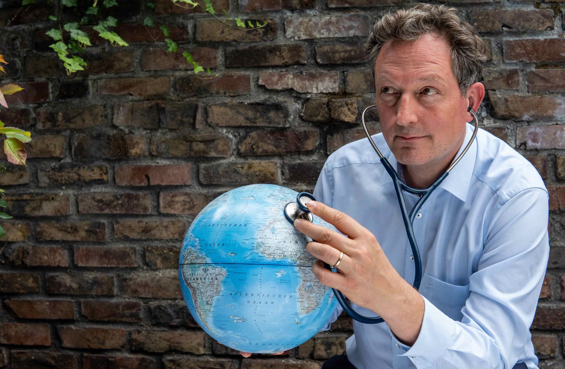 Eckart von Hirschhausen hält ein Stethoskop an einen Globus.