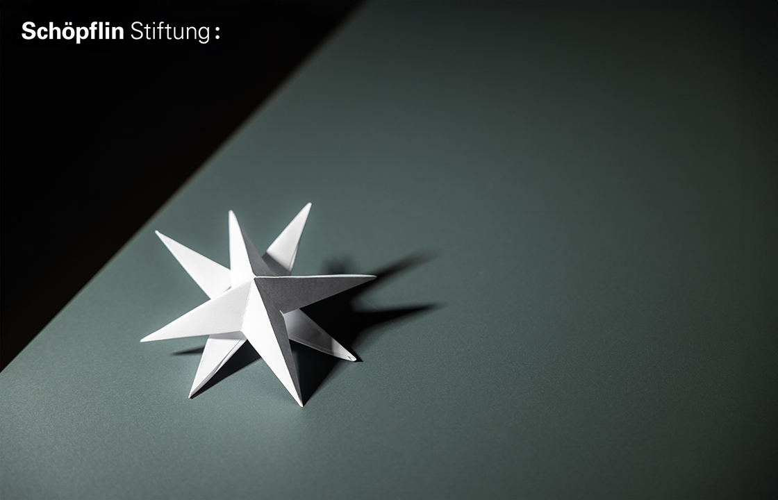 Ein weißer Papierstern auf einem Tisch, darüber das Logo der Schöpflin Stiftung..