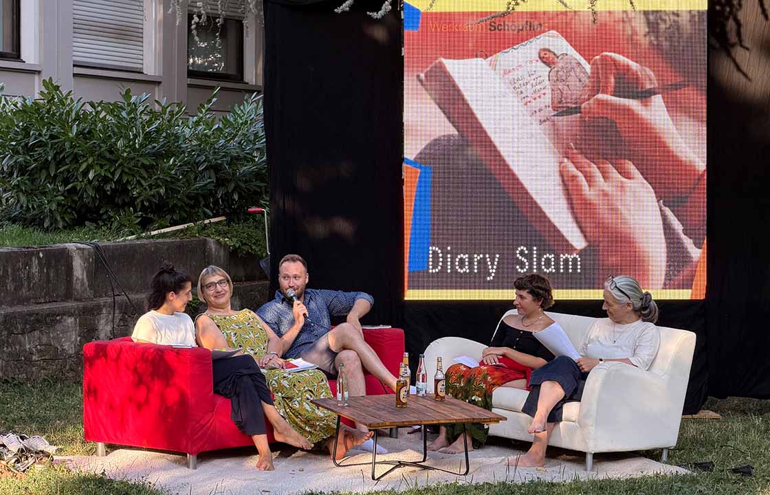 Fünf Personen sitzen auf Sofas im Freien vor einer großen Leinwand, die ein Tagebuch zeigt
