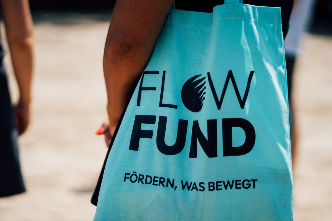 Eine Person trägt eine türkisfarbene Tasche mit der Aufschrift Flow Fund